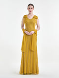 Woman wearing a mustard yellow dress with sheer sleeves on a white background