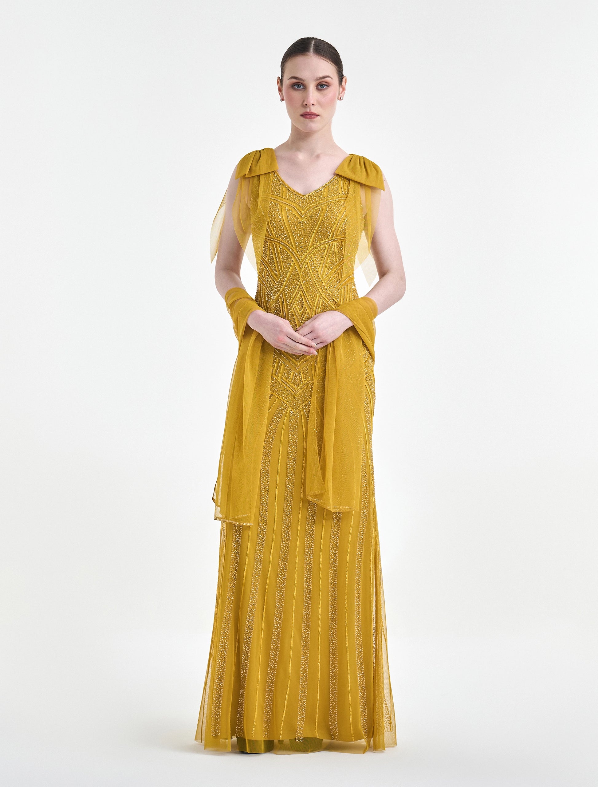 Woman wearing a mustard yellow dress with sheer sleeves on a white background